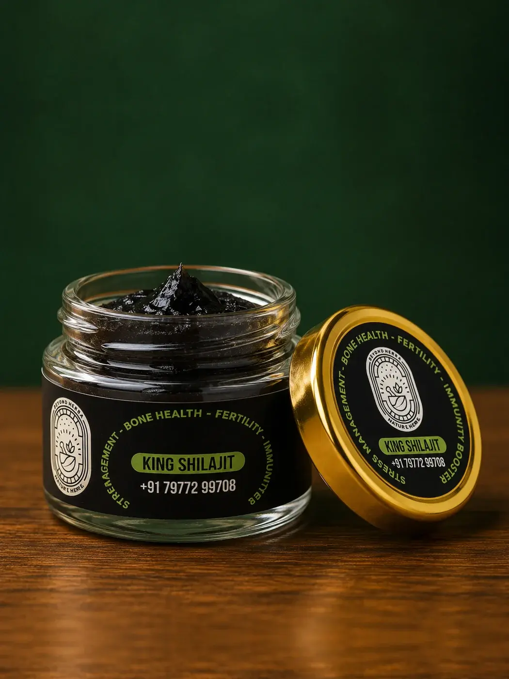 An open jar of Beyond Herba shilajit resin with its gold lid resting alongside, on a wooden surface against a dark green backdrop
